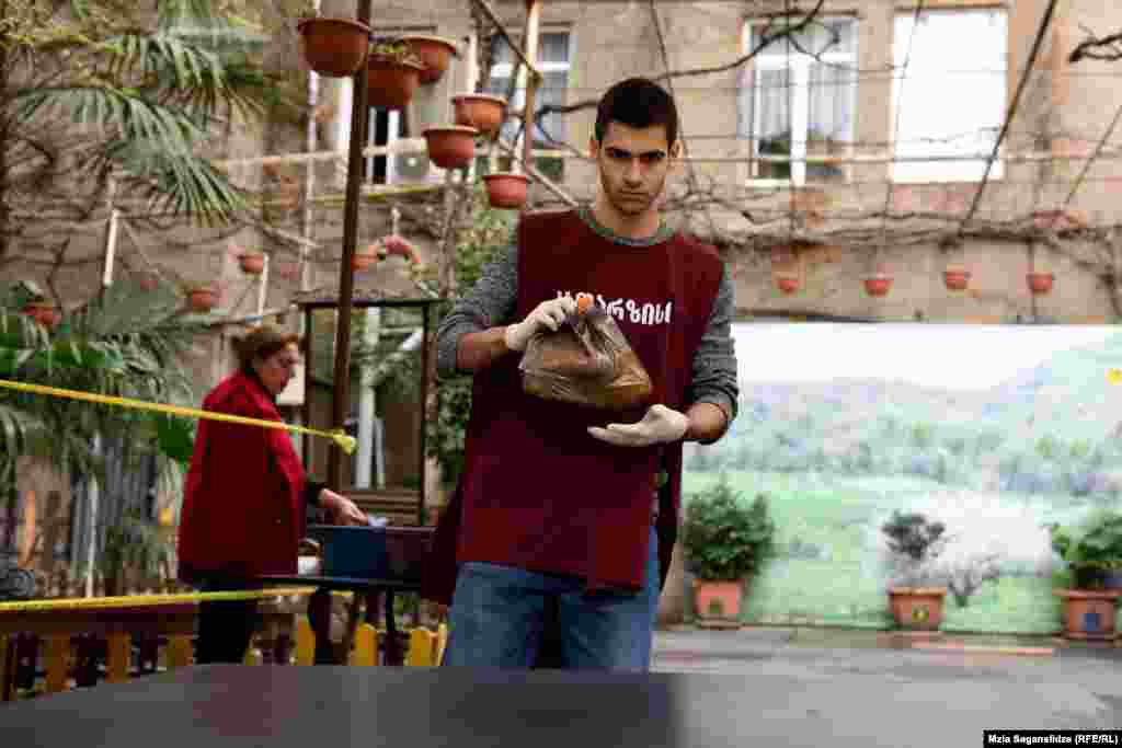 "კათარზისის" თანამშრომელი საკვების თითო პორციას მაგიდაზე დებს.