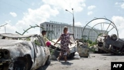 Жители Андижана проходят мимо сожженных автомобилей после столкновений, когда войска стреляли в демонстрантов.