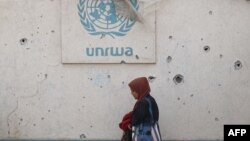 O femeie palestiniană trece pe lângă un zid deteriorat din Rafah, care poartă sigla UNRWA în Rafah, în sudul Fâșiei Gaza. Fotografie de arhivă. 