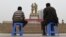 China - TO GO WITH CHINA-XINJIANG-UNREST-MIGRATION-POPULATION BY BENJAMIN HAAS   This photo taken on April 16, 2015 shows a Uighur man and boy watching a performance under a statue of late communist leader Mao Zedong meeting with a Uighur, in the central 
