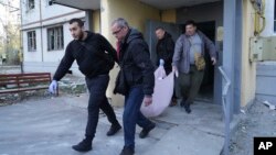 Oameni scoțînd trupul neînsuflețit al unui locuitor din Harkov dintr-un bloc de locuințe avariat de o lovitură rusească, 18 aprilie 2025 