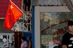 Residents stand near barbwired fences and a Chinese national flag in a community in Peyzawat, in China's Xinjiang region.