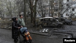 Banorët kalojnë pranë makinave të djegura në vendin e sulmit me dronë rusë në Dnipro, Ukrainë, 9 prill 2025.