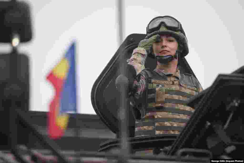 Un militar femeie, aflată într-o mașină de luptă, salută conducerea Armatei Române și invitații la parada militară de ziua națională a României, în București.