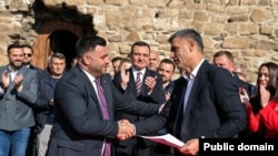 Sylejman Meholli i Lëvizjes Vetëvendosje (majtas) duke shtrënguar duart me Xhafer Tahirin e Lidhjes Demokratike të Kosovës, pas arritjes së koalicionit për balotazhin e 9 nëntorit në Vushtrri. Kryeministri në detyrë i Kosovës, Albin Kurti, shihet mbrapa duke duartrokitur. 