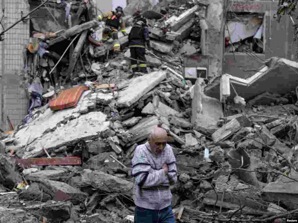 Жергиликтүү жашоочу көп кабаттуу үйдүн алдында турат. Куткаруучулар анын уранды алдында калган апасын издешүүдө. Үй орусиялык авиасоккудан кийин кыйраган. Фронт линиясындагы Константинова шаары. Донецк облусу, Украина. 8-май. 