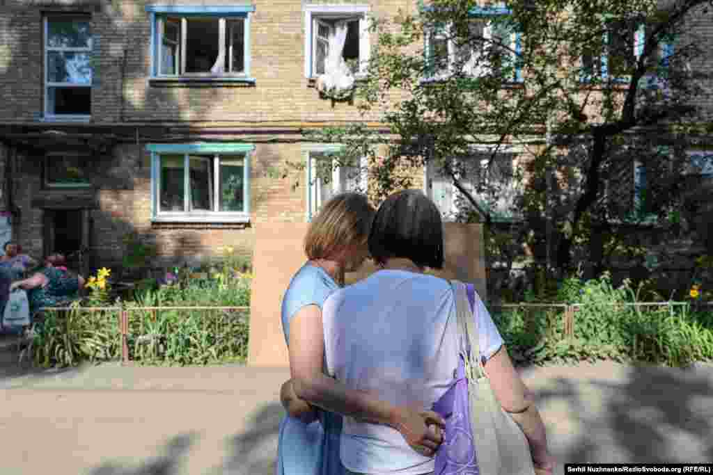 Жінки обіймаються біля будинку з вибитими через обстріл вікнами. Подільський район Києва, 10 липня 2025 року.