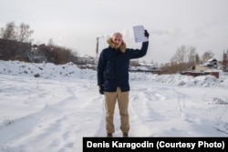 Denis Karagodin, holding the document showing who killed his great-grandfather, stands at the place where he believes he is buried in a mass grave along with some 15,000 other victims of the Great Terror.