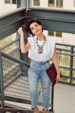 Safia pairs her simple t-shirt and jeans with an Afghan tribal coin necklace, originating from the Kuchi nomads of Afghanistan. She adds a red Afghan rug inspired clutch to finish her east meets west look.