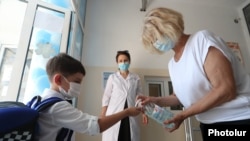 Armenia -- A teacher pours disinfecant onto the hands of a student entering a private school in Yerevan, September 1, 2020.