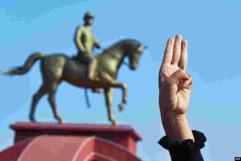 Протестувальник демонструє жест-символ опору військовому перевороту під час демонстрації в Найп'їдо. Позаду пам'ятник генералу Аун Сану, покійному батькові фактичної лідерки М'янми Су Чжі&nbsp;