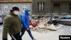 Люди проходят мимо поврежденных землетрясением автомобилей. Загреб, Хорватия,, 22 марта 2020 года.