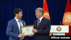 Президент Алмазбек Атамбаев 17-Азия оюндарынын коло байгесинин ээси Догдурбек уулу Эламанга  (эркин күрөш) акчалай сыйлыктын сертификатын тапшырууда. 22-октябрь, 2014-ж. 
