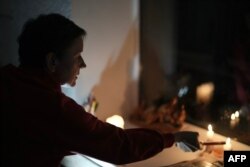 Olena, din Cernihiv, aprinde lumânări în apartamentul său în timpul unei întreruperi de curent electric, pe 22 octombrie 2025.