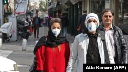 People wearing protective masks walk along a street in the Iranian capital, Tehran, on February 24.