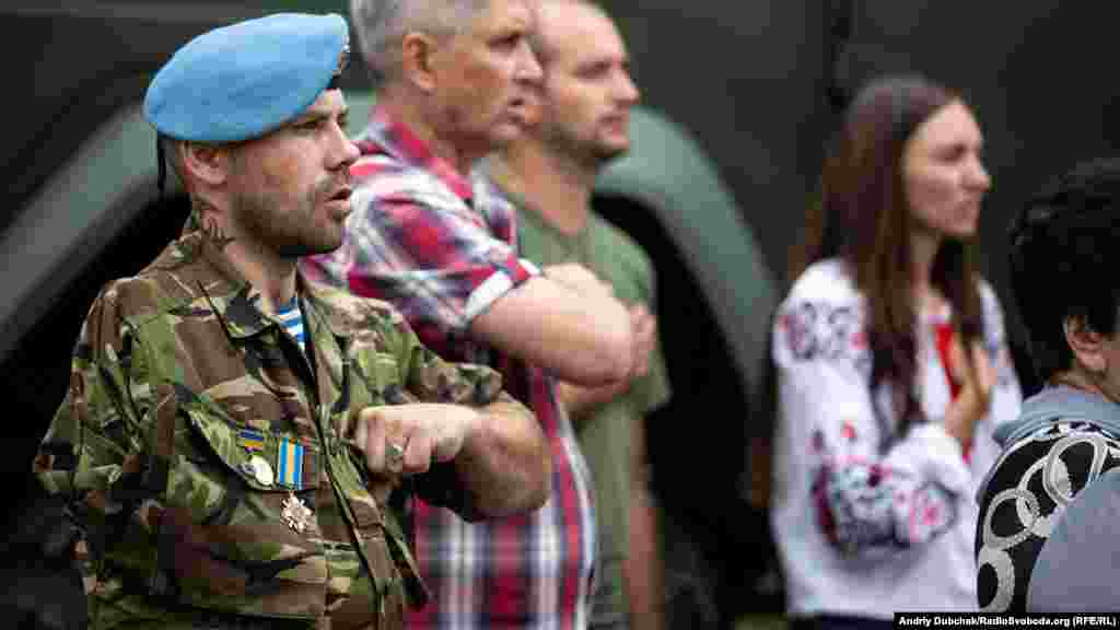 Роман Генецький, воїн 28-ї ОМБР, співає Гімн України. 26 серпня 2015 року під Мар&rsquo;їнкою у машину, за кермом якої він був, влучила 120-міліметрова міна. Хлопцеві вирвало суглоб плеча та 18 сантиметрів кістки, осколки пройшли крізь легені та щелепу. Зараз він потроху відновлюється