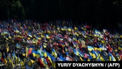 Местные жители стоят среди флагов во время церемонии похорон украинских военнослужащих, иллюстративное фото 