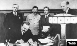 Міністр закордонних справ СРСР В'ячеслав Молотов підписує Договір про ненапад між СРСР і Німеччиною. Стоять (зліва направо) Йоахім фон-Ріббентроп, Йосип Сталін, В.М. Павлов, Ф. Гаус. Москва, 23 серпня 1939 року