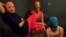 The three Pussy Riot members gathered in a darkened studio, with all three wearing the brightly colored stockings and the group's requisite balaclavas in gold, orange, and blue.