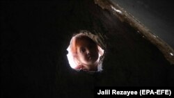 O fată afgană strămutată pozează pentru o fotografie lângă un adăpost temporar, în timp ce ea și alții așteaptă ajutor de la autorități la periferia orașului Herat, Afganistan, 15 iunie 2021.