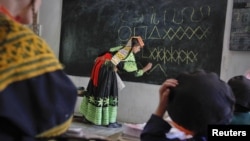 A teacher writes letters from the Kalasha alphabet on a blackboard.