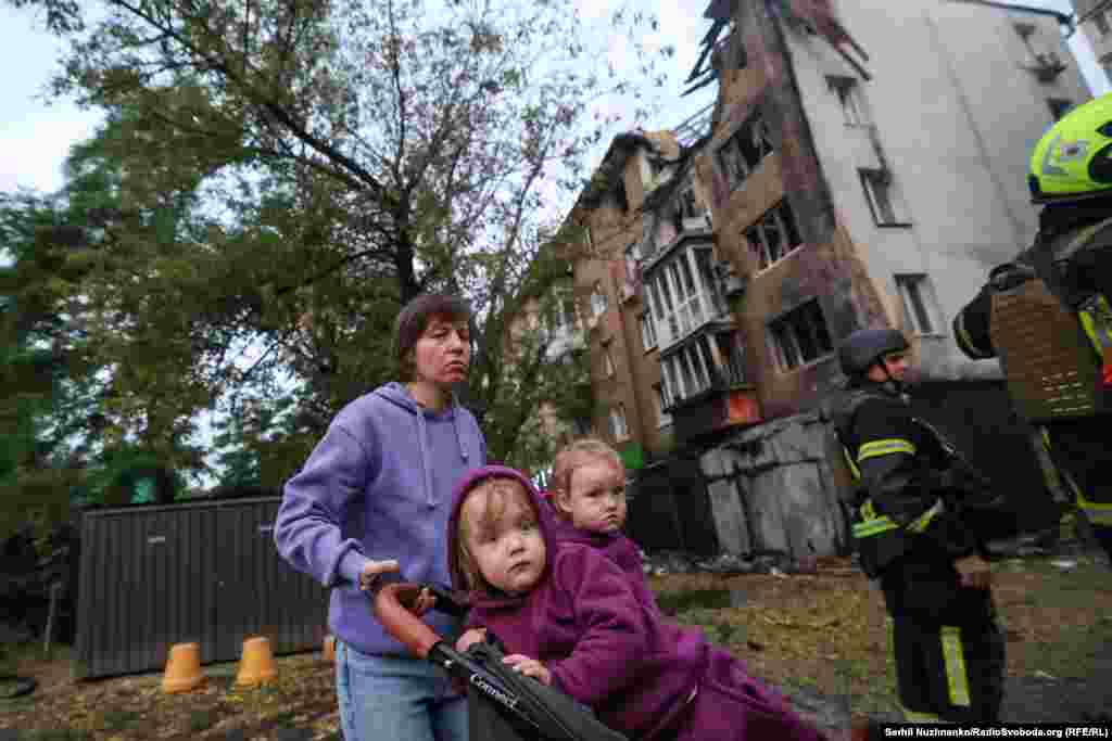 Жінка з двома дітьми на тлі пошкодженого будинку