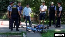 Полицейские стоят над задержанным мужчиной на месте нападений в центре Алматы. 18 июля 2016 года.  