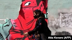 An Iranian woman wearing a protective mask walks past mask graffiti in Tehran.