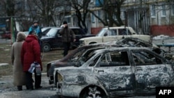 People look at burned-out cars as they walk along a street in the southern Ukrainian city of Mariupol, which was heavily shelled on January 24. 