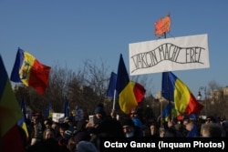 „Vakcin macht frei” de pe pancarta manifestanților anti-restricții din Piața Victoriei parafrazează mesajul macabru care îi întâmpina pe victimele Holocaustului la Auschwitz „Arbeit macht frei”/ „Munca vă va face liberi”. Ca detaliu semnificativ, deținuții evrei care au fost obligați să facă poarta de fier forjat erau artiști și arhitecți Bauhaus, stil marcat în întreaga Europă de artiști evrei, foarte apreciat și astăzi. Victimele l-au folosit ca un subtil gest de rezistență contra călăilor lor.
