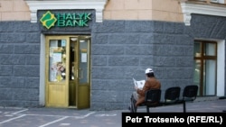 Мужчина читает газету рядом с отделением коммерческого банка в Алматы