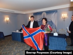 Anna Netrebko și așa-zisul lider separatist Oleg Tsarev cu steagul „Novorossiya”, un teritoriu nerecunoscut internațional, la conferința de presă în care diva operei ruse a decis să doneze bani teatrului din Donețk, în decembrie 2014.
