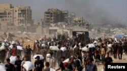 Газанын тургундары гуманитардык жардам таратылгандан кийин азык-түлүк жана башка жардам салынган мүшөк көтөрүп баратышат. 27-июль, 2025-жыл 