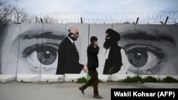 FILE: A man walks past a wall painted with images of U.S. Special Representative for Afghanistan Reconciliation Zalmay Khalilzad (L) and Taliban co-founder Mullah Abdul Ghani Baradar.