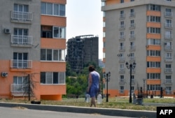 Жінка несе бутлі з водою, окупований Маріуполь, 14 липня 2025 року