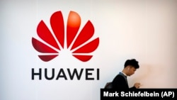 Un bărbat își folosește smartphone-ul în timp ce stă lângă un panou publicitar pentru firma chineză de tehnologie Huawei (ilustrație generică).