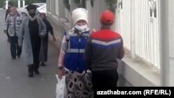 Aşgabadyň köçesinden barýan ýüzi maskaly adamlar.