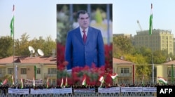 Люди размахивают таджикскими флагами перед гигантским плакатом с изображением президента Таджикистана Эмомали Рахмона во время митинга в поддержку Рахмона в Душанбе, 3 ноября 2013 г.