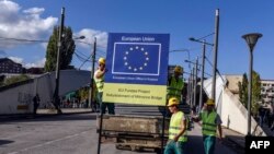 Punëtorë të ndërtimit afër pllakës që tregonte se rivitalizimi i urës kryesore mbi Ibër është financuar prej BE-së. 17 tetor 2015. (Foto: AFP)