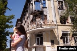 Мама з дитиною біля будівлі в Маріуполі, зруйнованої внаслідок бойових дій