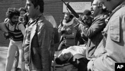 აიათოლას ერთგულ მომხრეები. აშშ-ის საელჩოდან სროლისას დაჭრილი ადამიანი საკაცით გამოჰყავთ.