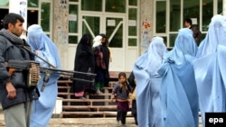 Афганский полицейский охраняет женщин в парандже, покидающих семинар по домашнему насилию в Герате. 24 ноября 2009 года