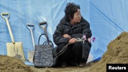 Токико Абе, жительница Хигаси Мацусима, в ожидании тела погибшего мужа у свежевырытой могилы. Фото REUTERS/Yuriko Nakao. 2011.