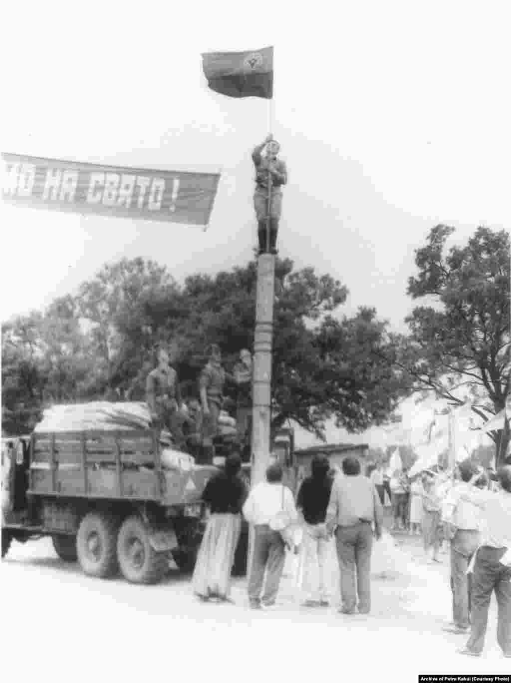 На фото військові допомагають встановити червоно-чорний прапор із емблемою ОУН(р) на дерев'яному стовпі неподалік могили кошового отамана Запорізької Січі Івана Сірка