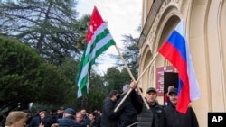 აფხაზეთის დე ფაქტო რესპუბლიკის "დროშა" და რუსეთის დროშა საპროტესტო აქციაზე სოხუმში. 2024 წლის 15 ნოემბერი