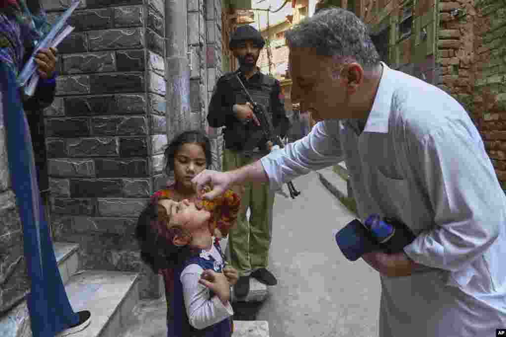 یک کارشناس بهداشت در حال تزریق واکسن پولیو به کودکی در حومه‌ٔ پیشاور در استان بلوچستان پاکستان، در حالی که یک پلیس نظاره‌گر است