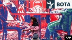 Një grua kalon pranë një murali që përshkruan një zyrtar iranian me veshje civile të ulur përballë një zyrtari amerikan me uniforma ushtarake, të pikturuar në muret e jashtme të ish-Ambasadës amerikane në Teheran.