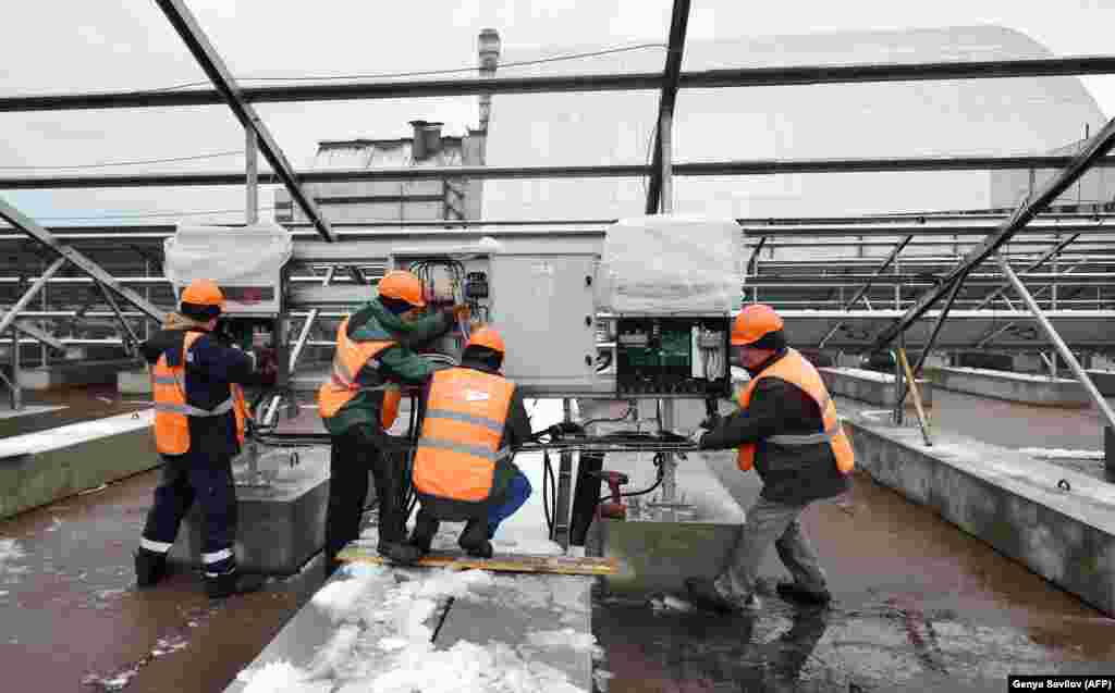 Рабочие подключают провода к электрощитам на месте будущей солнечной электростанции. На заднем плане &ndash; труба ядерного реактора, взорвавшегося в 1986 году. Авария на Чернобыльской АЭС стала одной из самых страшных ядерных катастроф.&nbsp;