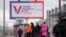 People wait at a bus stop next to a billboard promoting the upcoming presidential election in St. Petersburg in December.