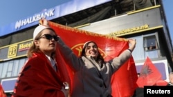 Një vajë e mbeshtjellë me flamurin kombëtar shqiptar dhe me plis në kokë merr pjesë përkrah një vajze tjetër me flamurin e UÇK-së në mbrojtje të ish-eprorëve të Ushtrisë Çlirimtare të Kosovës, në Sheshin “Skënderbeu” në Shkup, 13 dhjetor. 